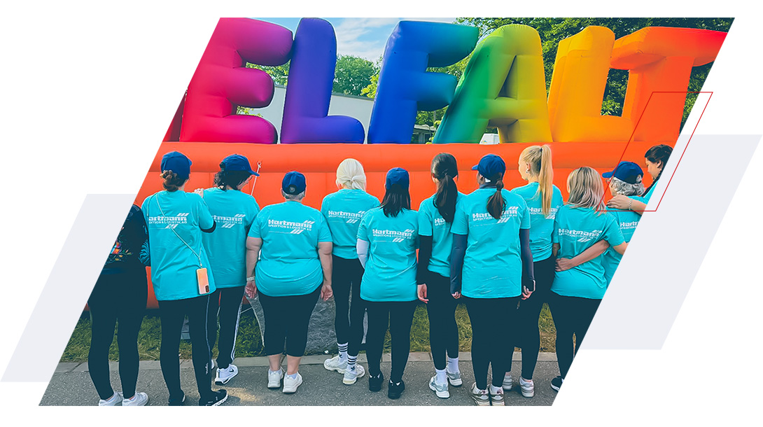 Hartmann-Laufteam beim B2Run Firmenlauf in Karlsruhe, von hinten in türkisfarbenen Shirts mit Hartmann-Logo vor dem bunten Zieleinlauf-Banner.