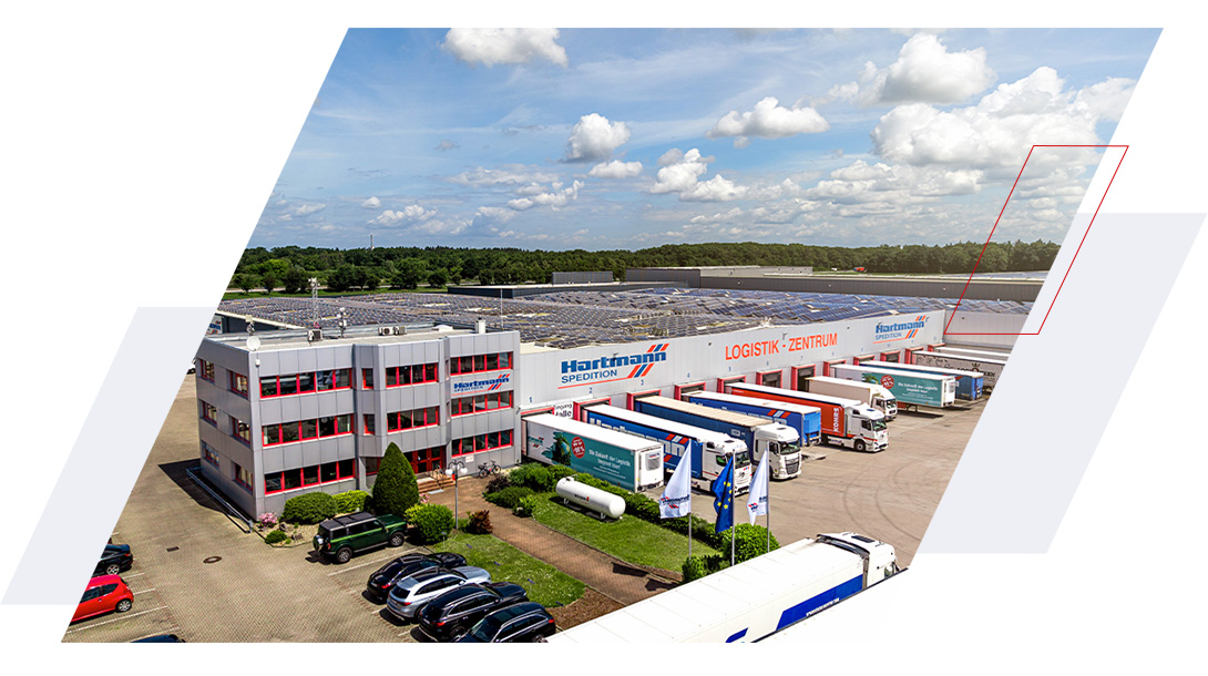 Luftaufnahme des Hartmann Logistikzentrums mit zahlreichen Lkw an den Laderampen und Solaranlagen auf dem Hallendach.