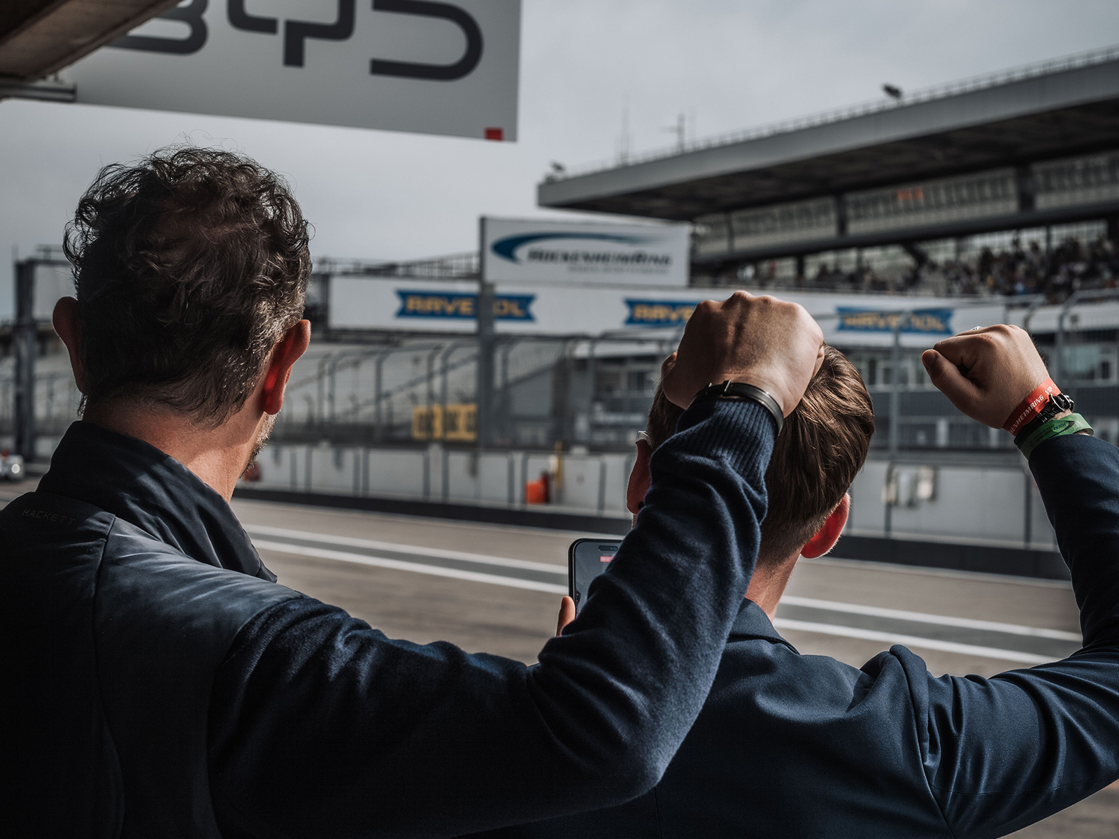 Zwei Männer jubeln an der Boxengasse des Hockenheimrings während eines Motorsport-Events.