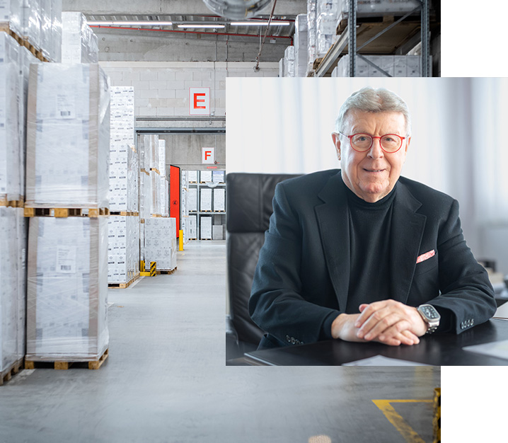 Porträt des Vorstandsvorsitzenden von Hartmann in einem Büro, kombiniert mit einer Lagerhalle mit palettierten Waren.