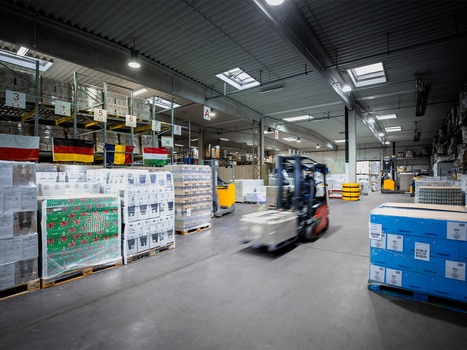 Gabelstapler transportiert palettierte Waren durch eine Lagerhalle von Hartmann mit Hochregalen und verpackten Lebensmitteln.